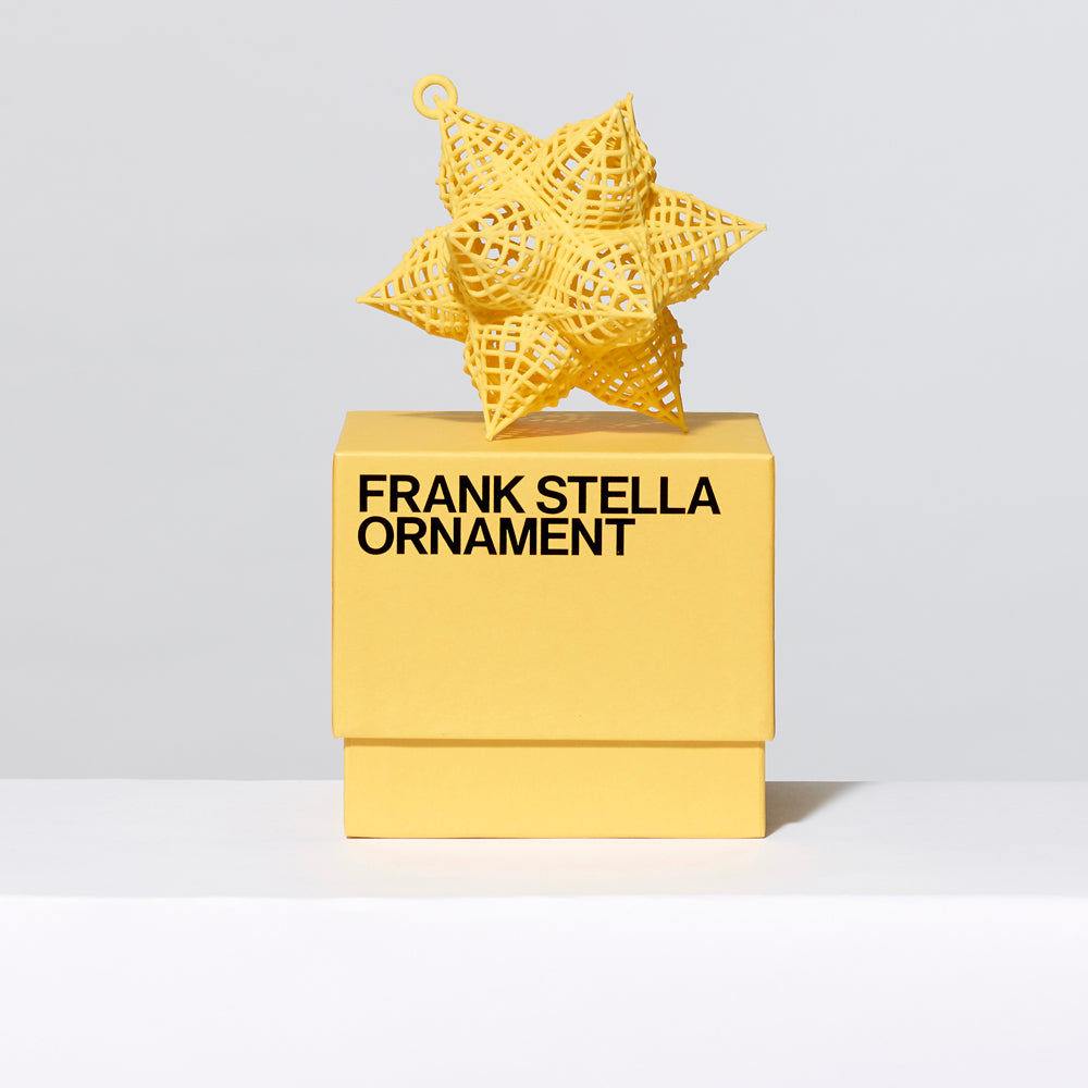 3-D printed plastic Frank Stella star ornament in yellow on top of gift box. Measures approximately 4" x 4" x 4"
