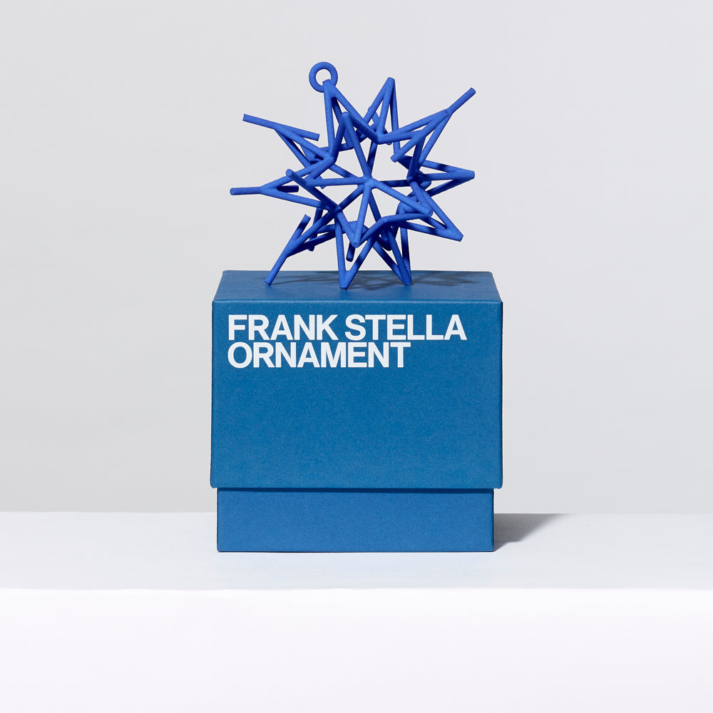 3-D printed plastic Frank Stella star ornament in blue on top of gift box. Measures approximately 4" x 4" x 4"