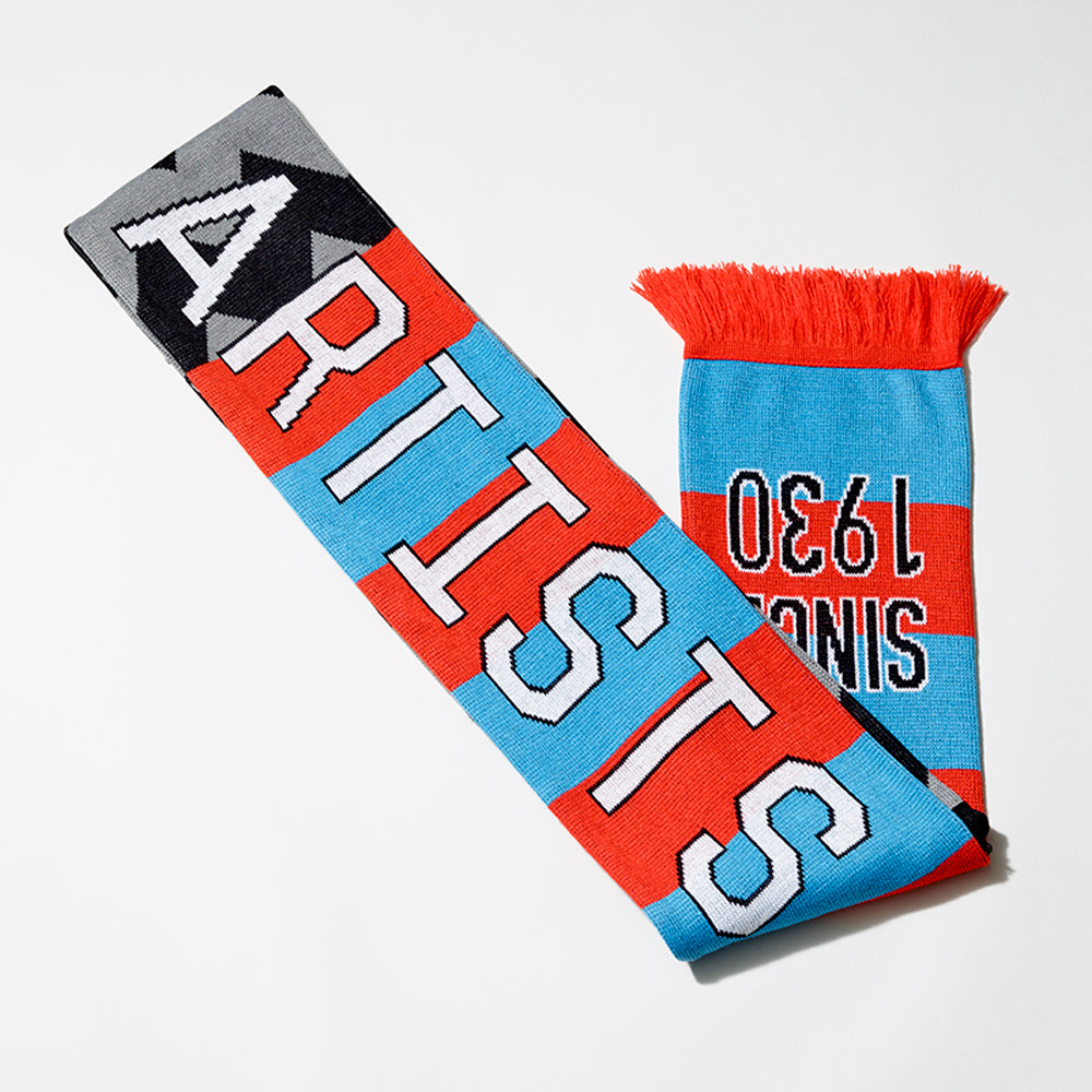 100% acrylic Whitney Cattelan football scarf in blue and red stripes and black and gray w's, with the word Artists in white text, and Since 1930 in black text. Measures 80" long and 7" wide. 