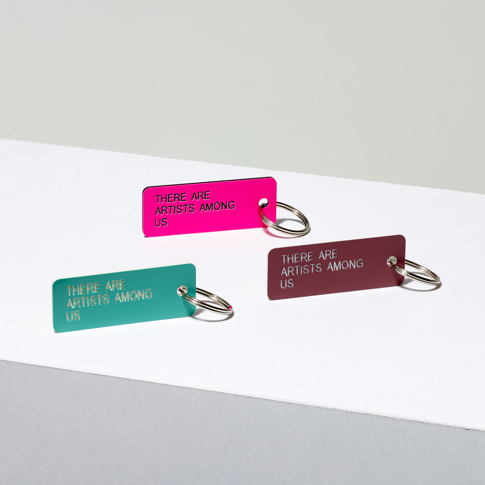 Assortment of etched acrylic keychains in various colors featuring the text "There Are Artists Among Us"