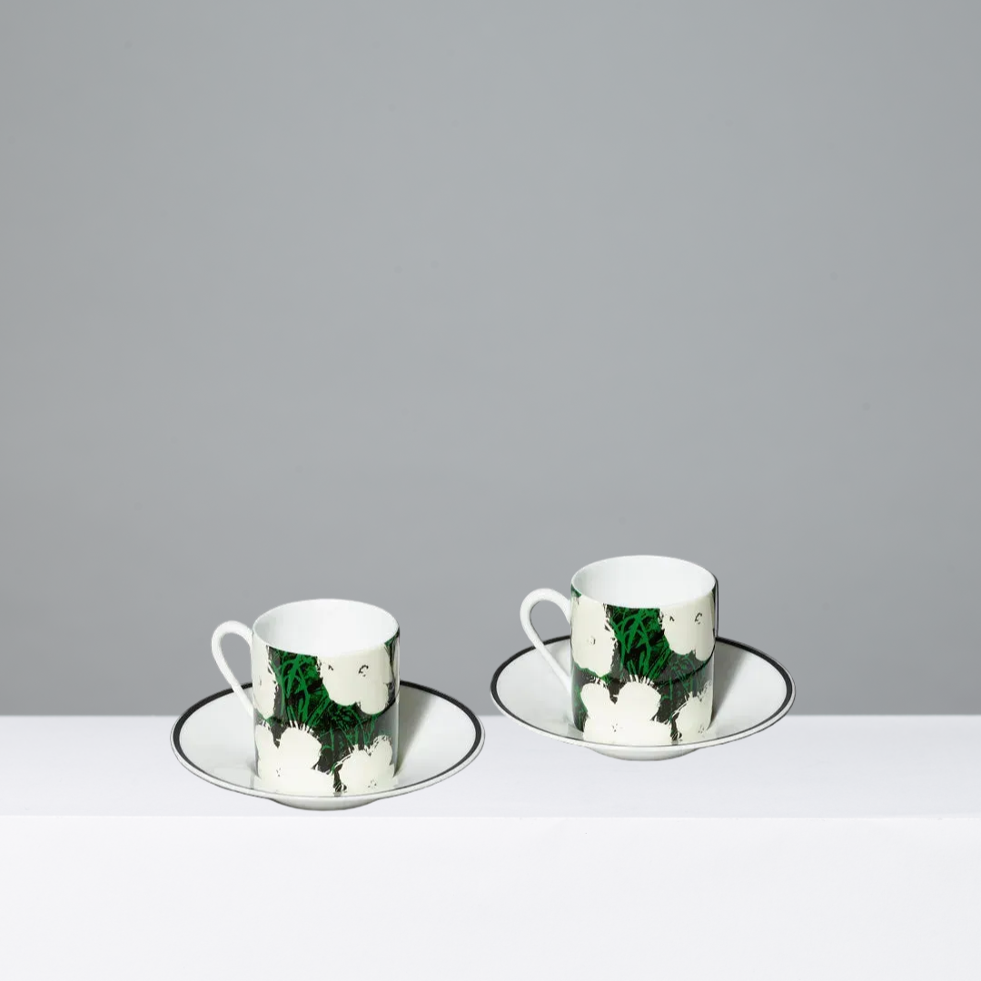 Two ceramic cups with saucers featuring Andy Warhol's White Flowers artwork on a gray background