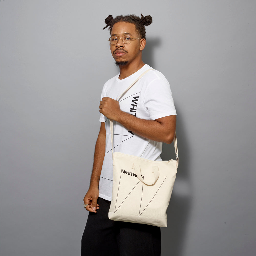 Model holding a 100% cotton canvas tote featuring the Whitney logo. Measures 13" x 13" 