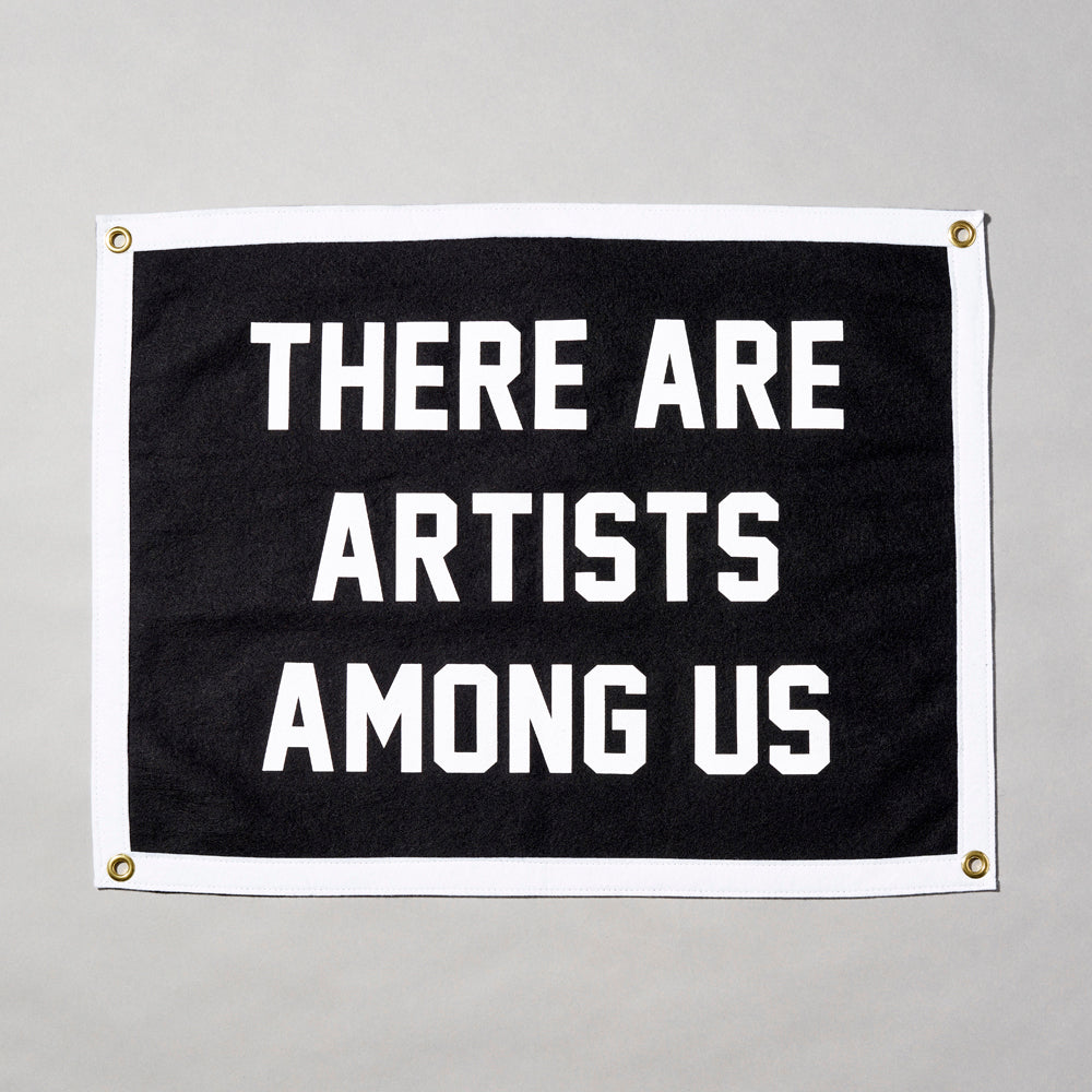 Screen printed felt camp flag with a white border and black body, featuring "There Are Artists Among Us" in white text. Measurements: 24" x 18".