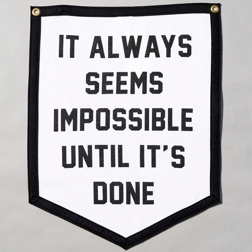 Screen printed felt flag with black border and white body. Text reads "It Always Seems Impossible Until It's Done" in black text. Measures 18" x 23