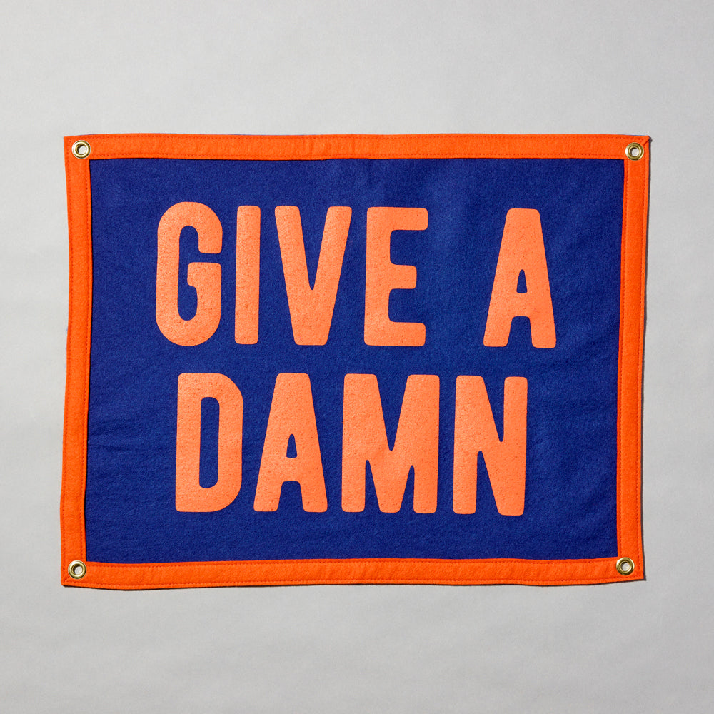 Screen printed felt camp flag with an orange border and blue body, featuring "Give A Damn" in orange text. Measurements: 24" x 18".