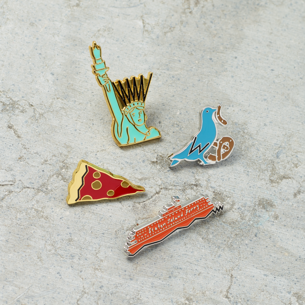 Assortment of hard enamel and metal pins illustrated by Tamara Shopsin, featuring iconic New York landmarks; Pigeon, Lady Liberty, Staten Island Ferry, and Pizza slice.