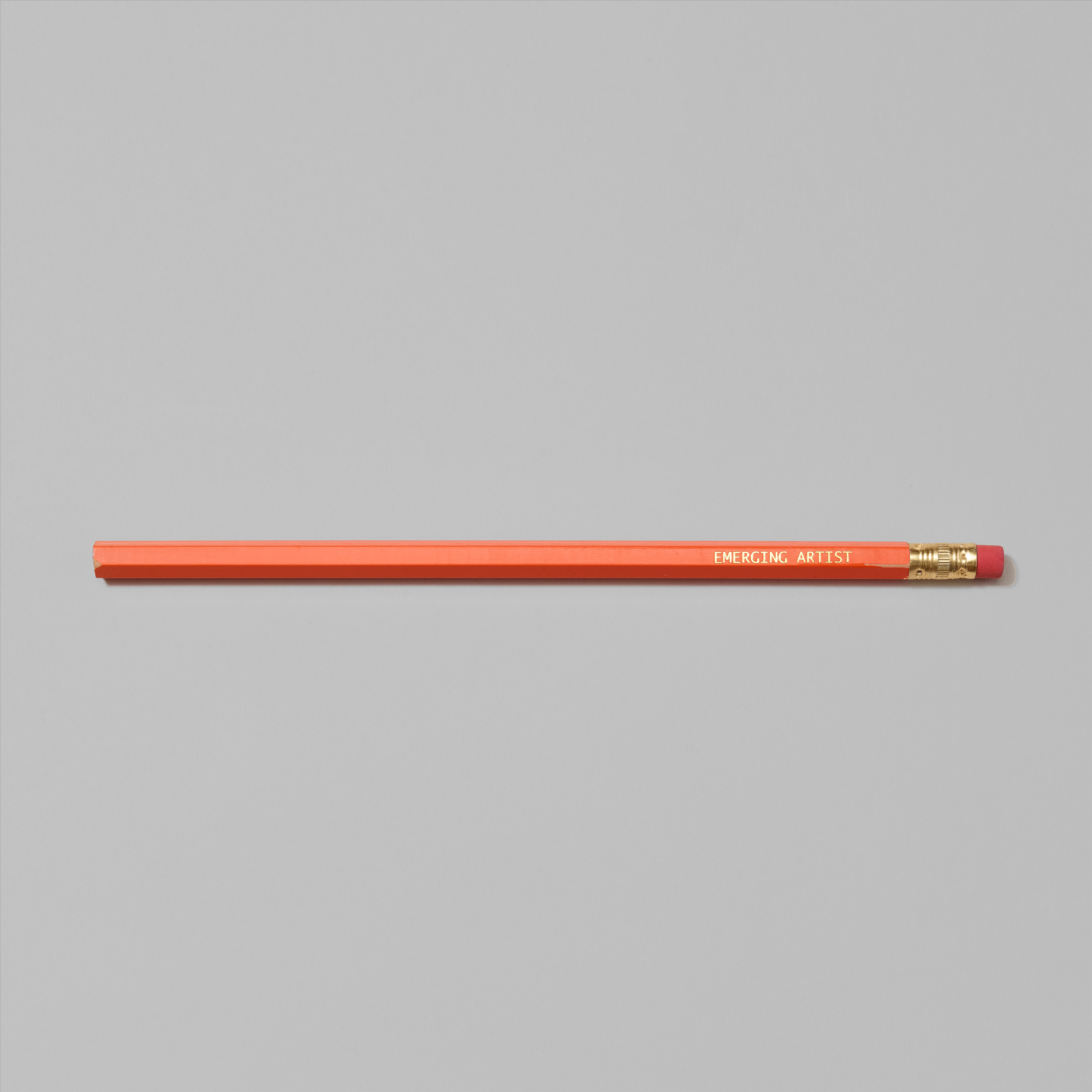 Orange pencil with Emerging Artist in gold foil text