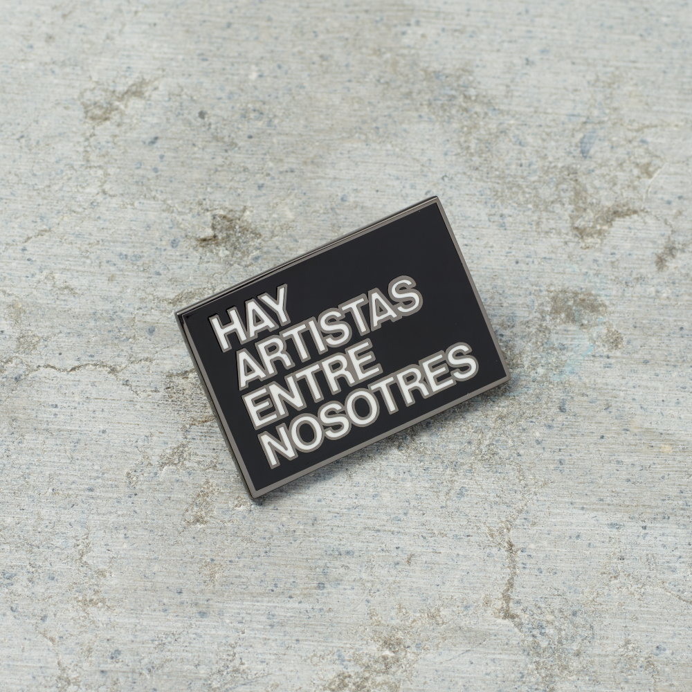 Black nickel plated brass and hard enamel pin that reads Hay Artistas Entre Nosotres