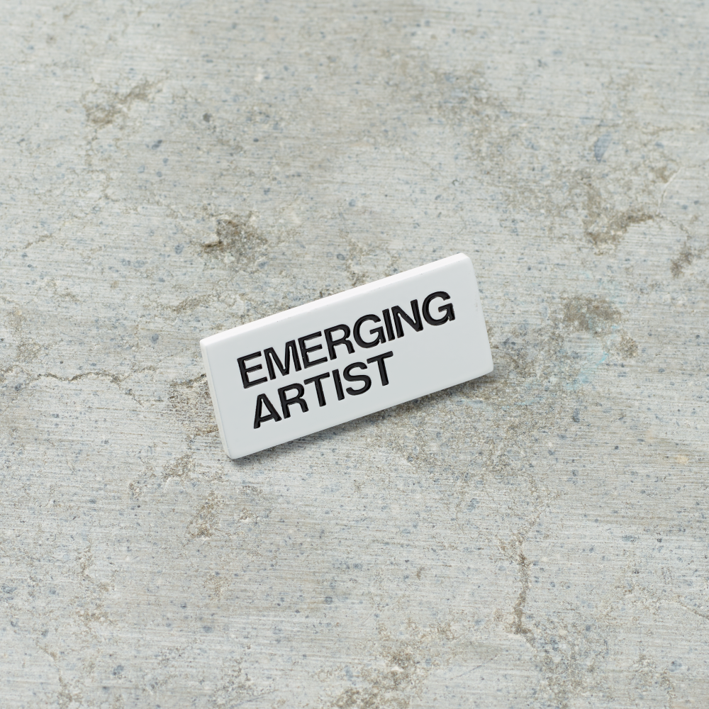 Black nickel plated brass and hard enamel pin that reads Emerging Artist