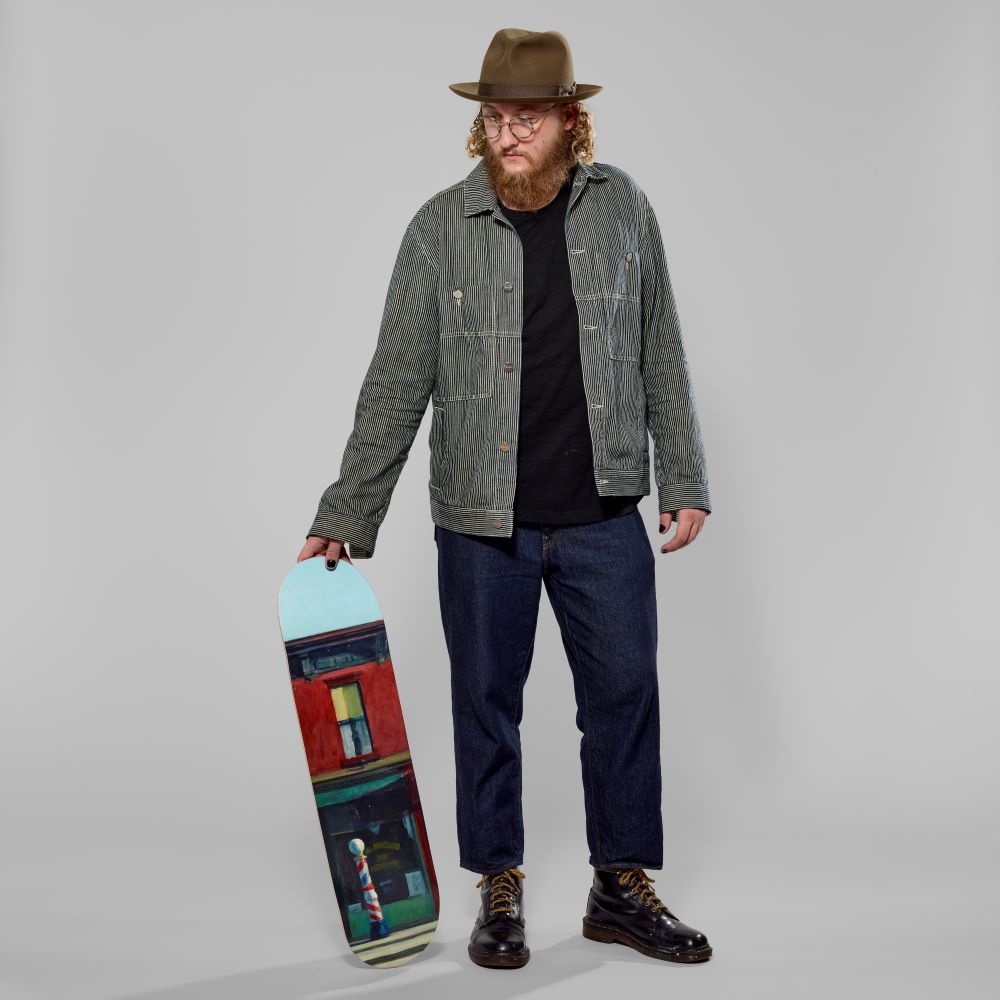 Model holding Maple wood skate deck featuring Edward Hopper's Early Sunday Morning. Measures 31" x 8" x .5".