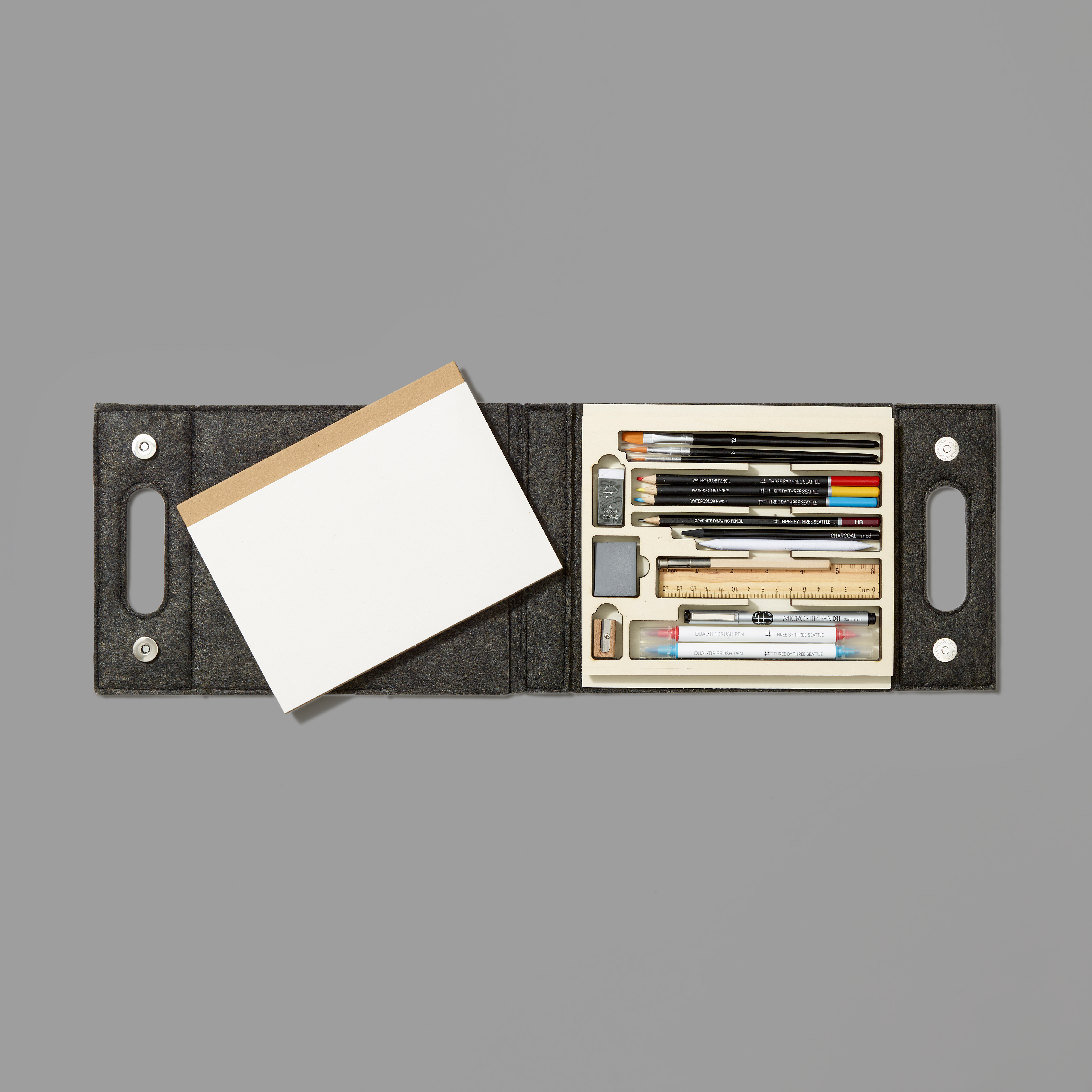 Set of art supplies including pencils, markers, and a notebook in a black case on a gray background