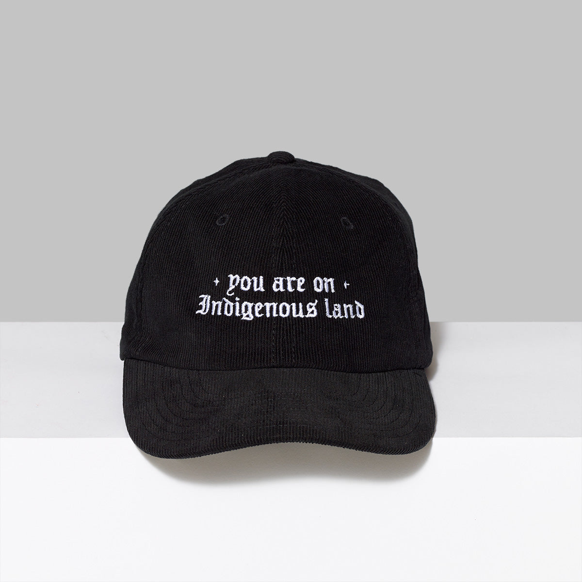 100% cotton corduroy black hat with +you are on Indigenous land+ embroidered in white