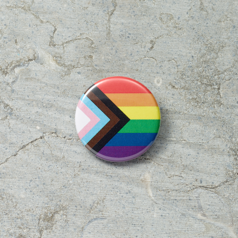 Round button with rainbow and black chevron pattern on a textured gray surface