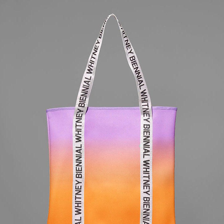 Gradient tote bag with 'Whitney Biennial' text on a gray background