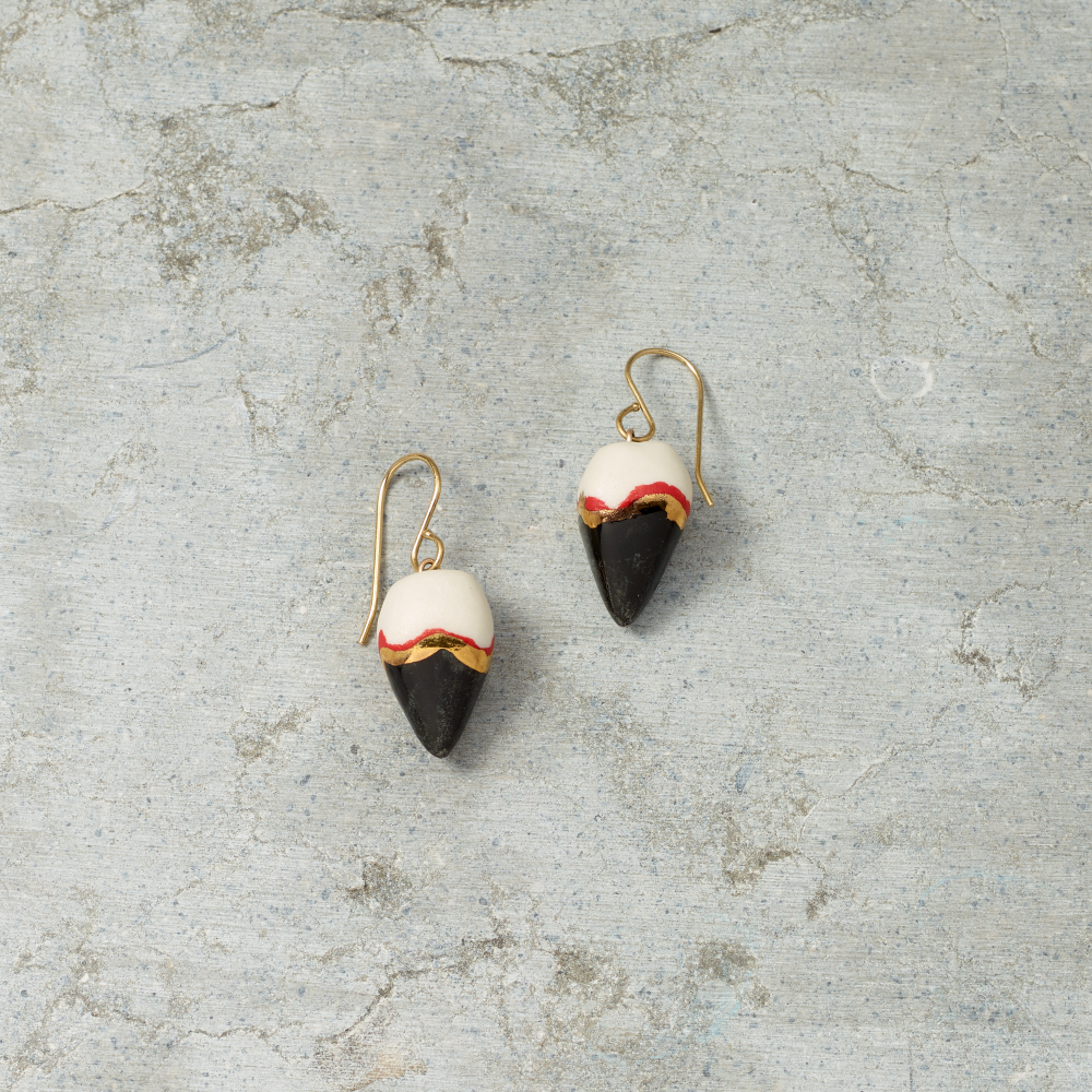 Pair of earrings with black, white, and gold design on a textured gray surface