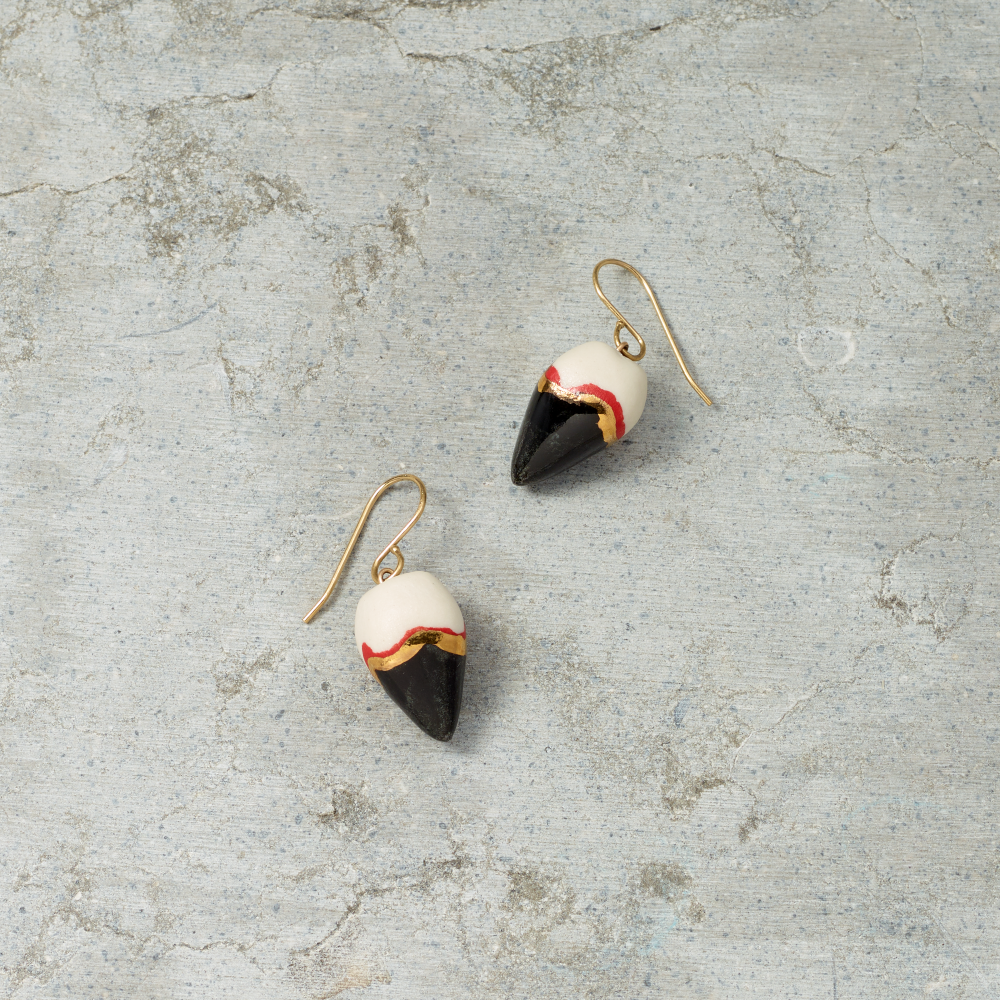 Pair of earrings with black, white, and gold design on a gray surface
