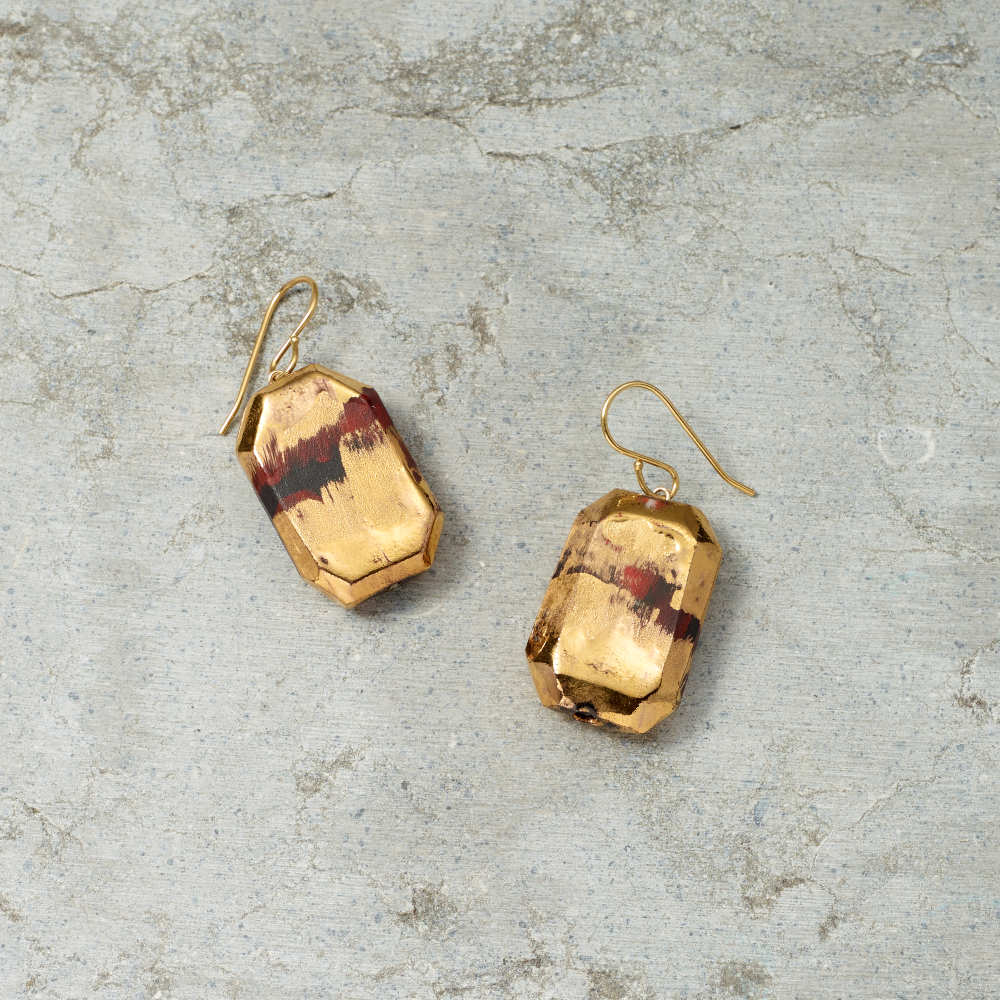 Gold earrings with red and black accents on a textured gray surface