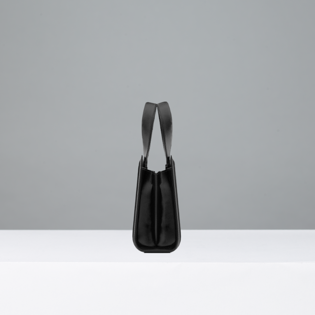 Side view of black leather handbag with thin straps on a gray background