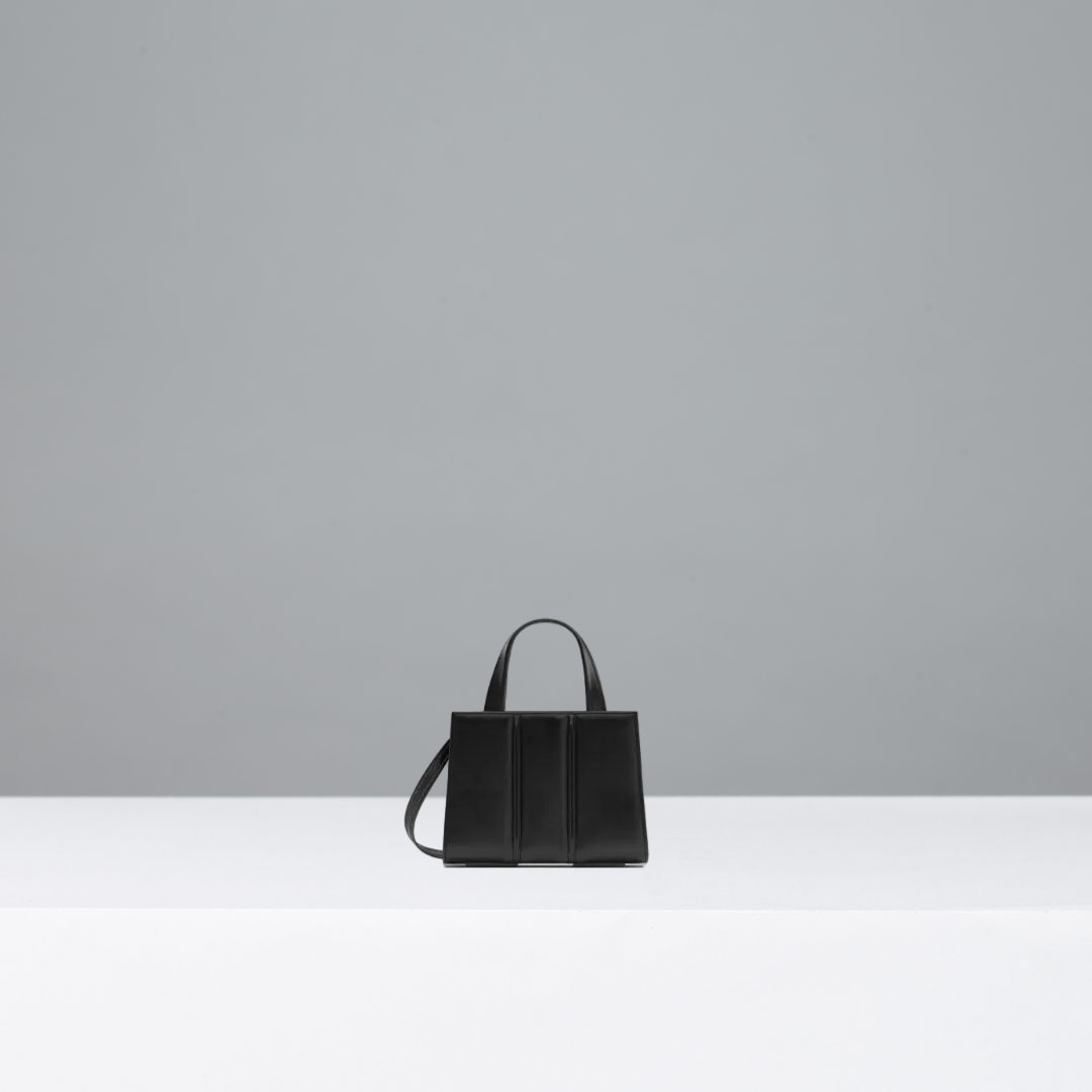Black handbag on a white surface with a gray background