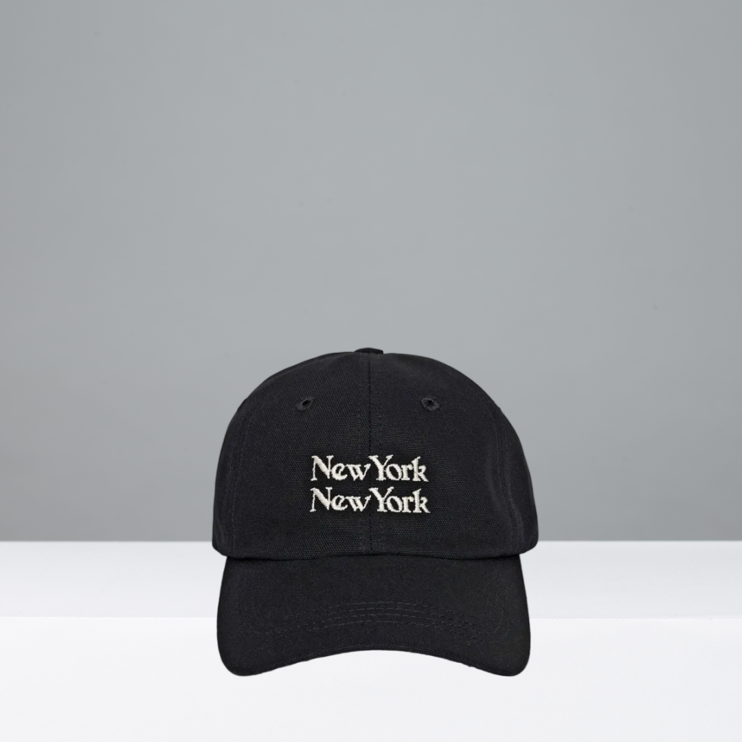 A black baseball cap with 'New York New York' embroidered in white gothic-style lettering on the front, displayed against a split gray and white studio background.