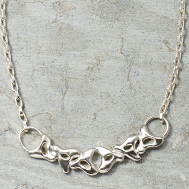 Silver necklace with inkblot-like design on a textured gray surface