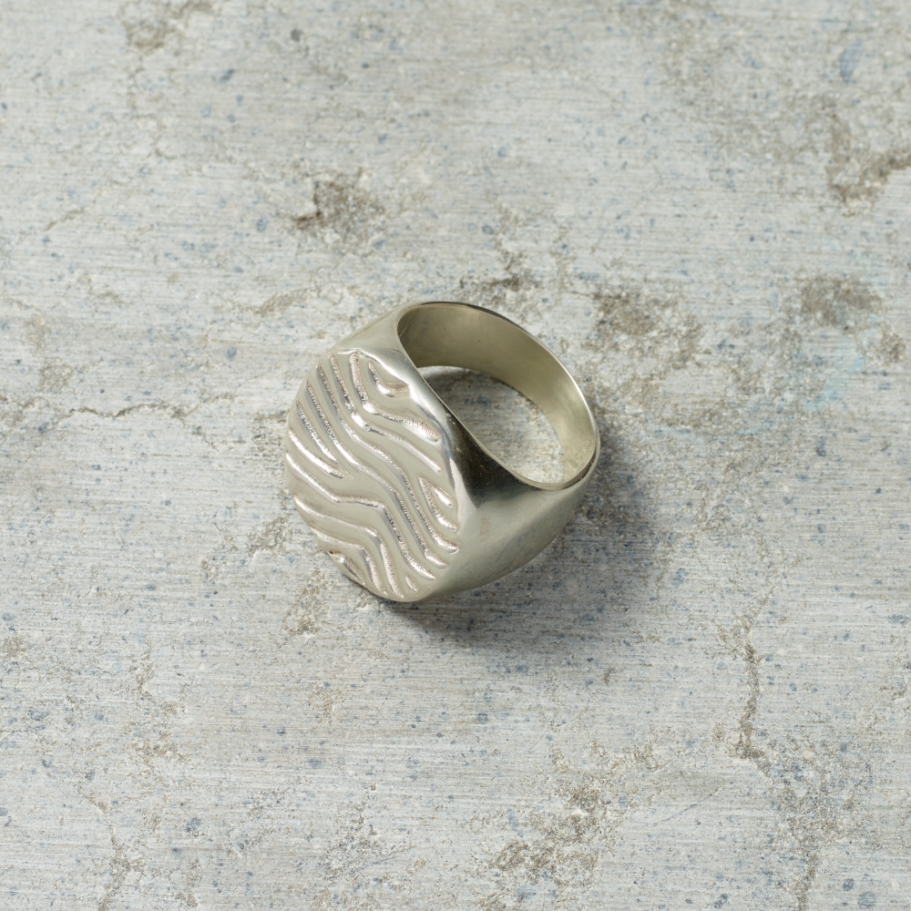 Silver ring with wavy design on a textured gray surface