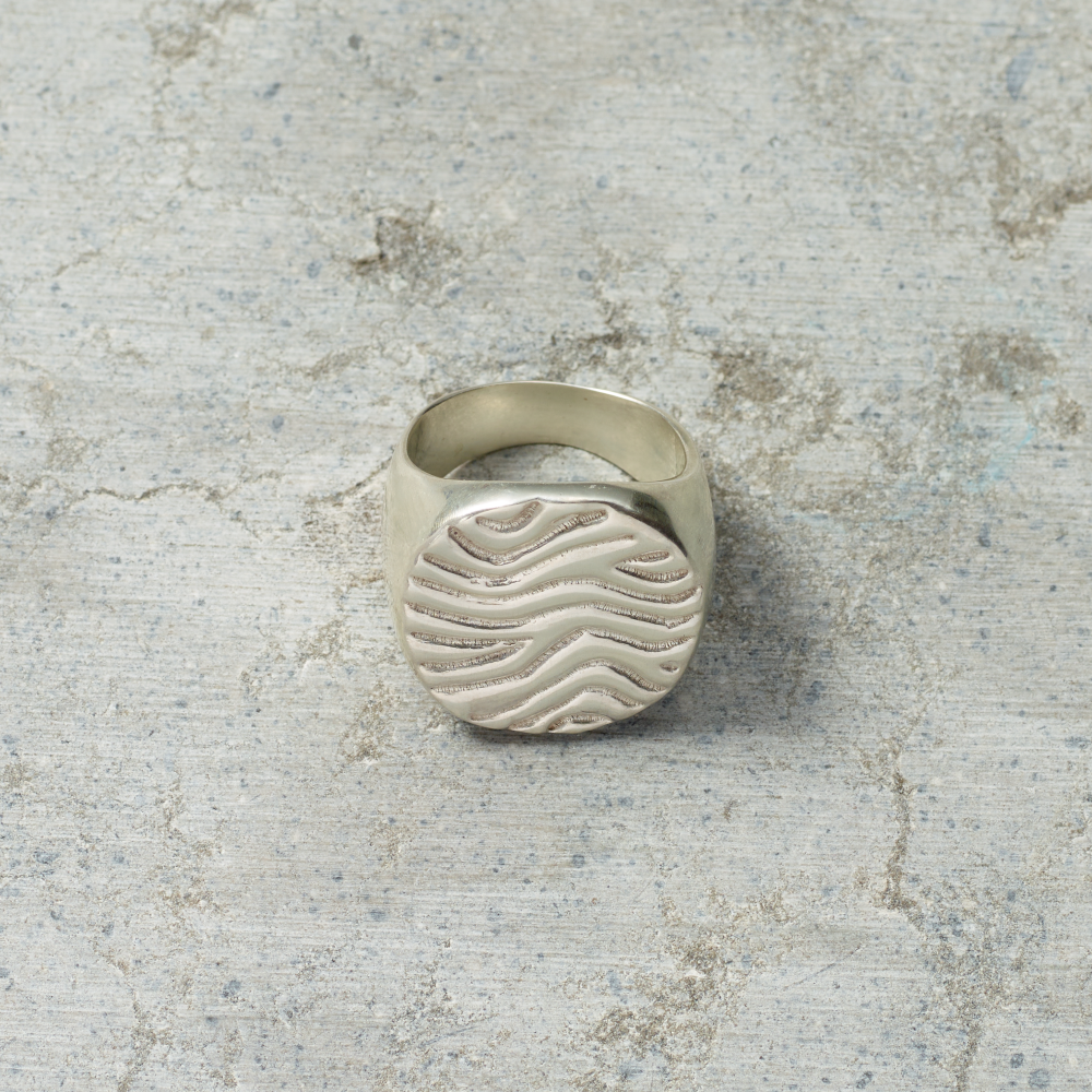 Silver ring with wavy design on a textured gray surface