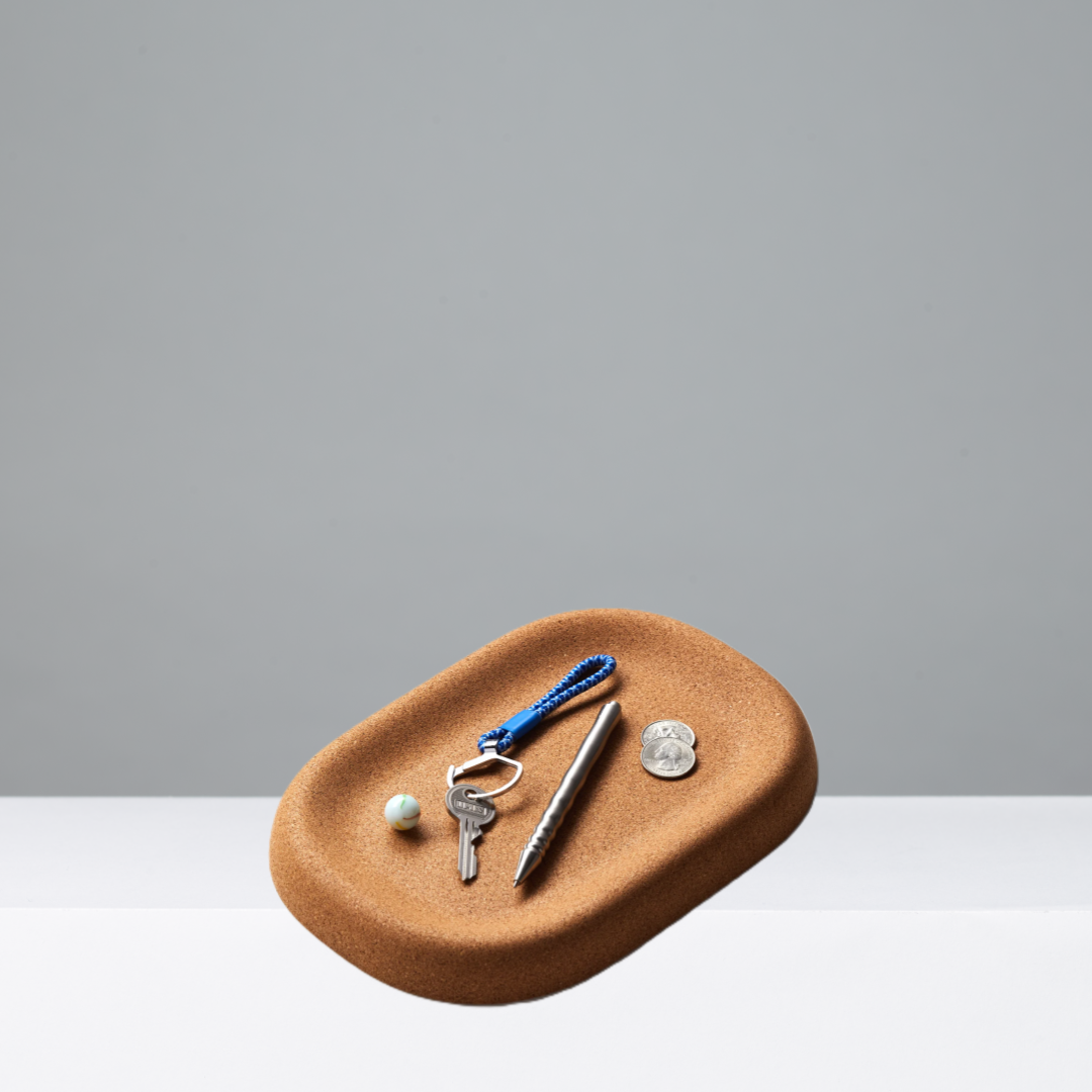Cork tray with keys, pen, and coins on a gray background