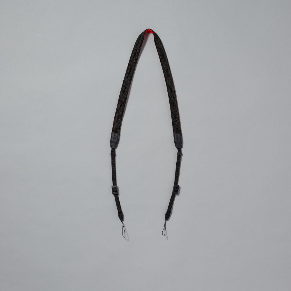 Black camera strap with red accent on a gray background