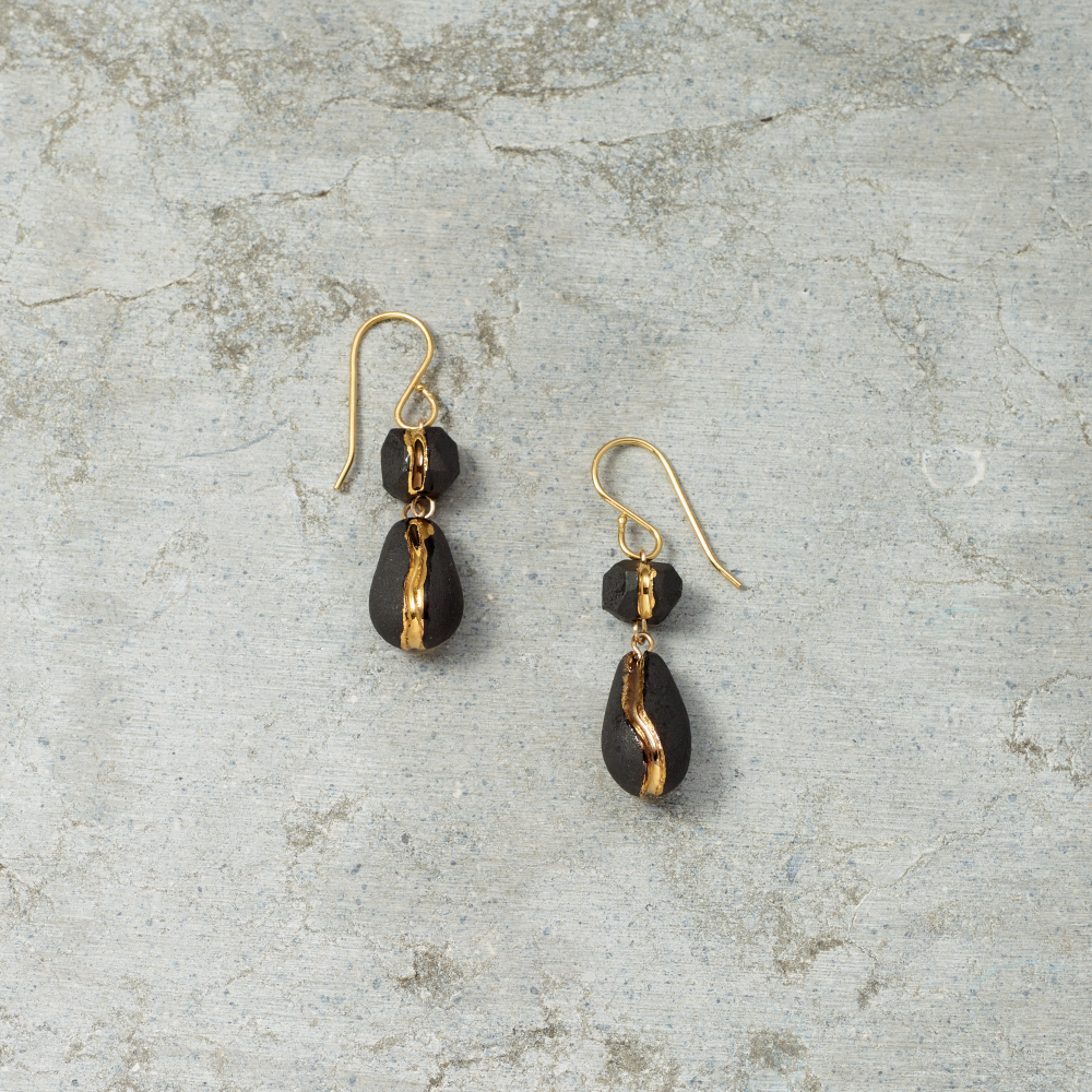 Pair of black teardrop earrings with gold accents on a textured gray surface