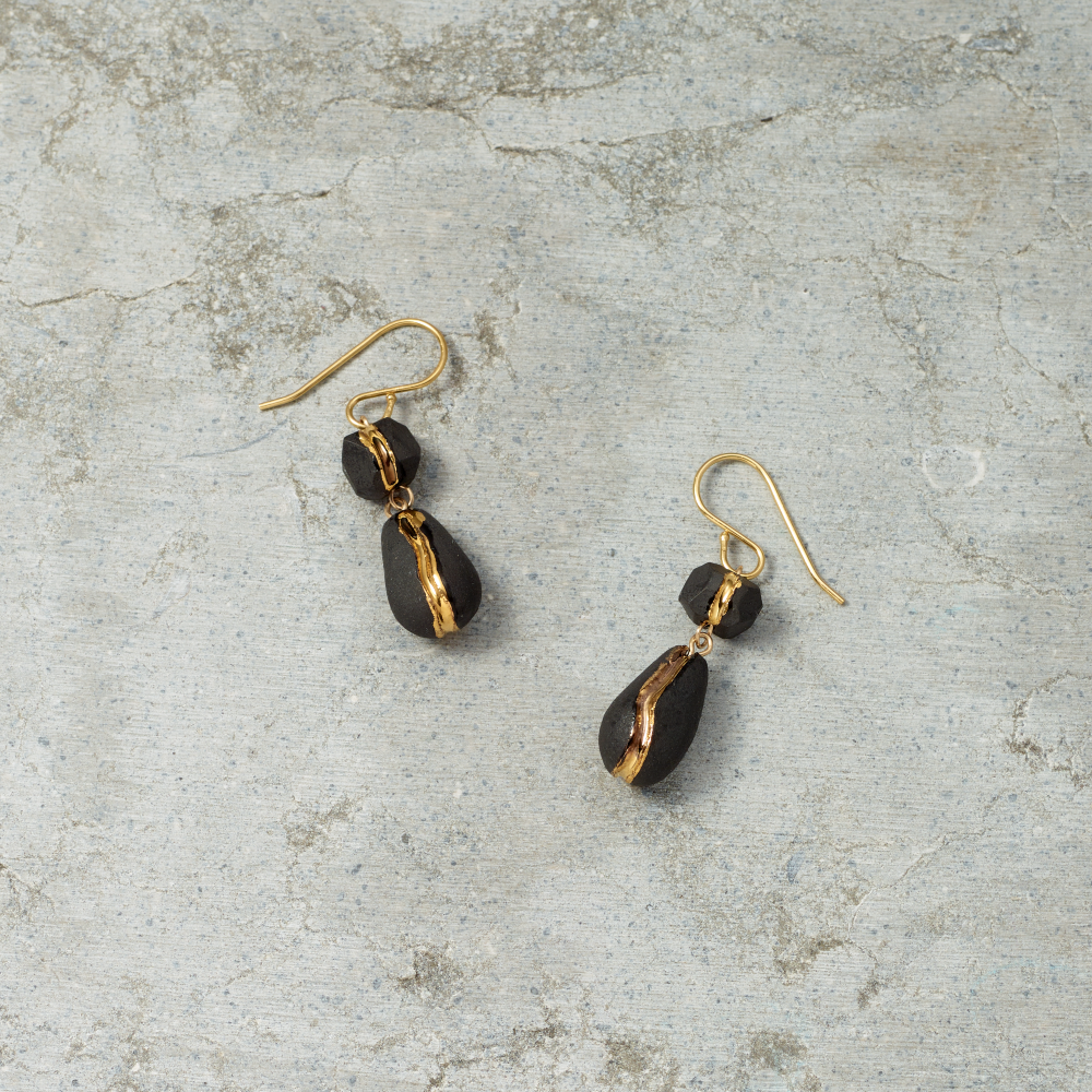 Pair of black teardrop earrings with gold accents on a textured gray surface