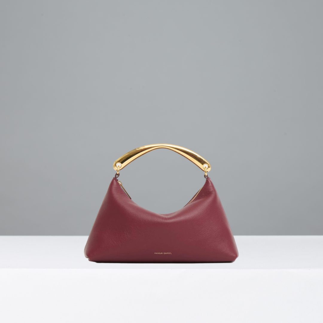 Oxblood red handbag with gold metal handle on a gray background