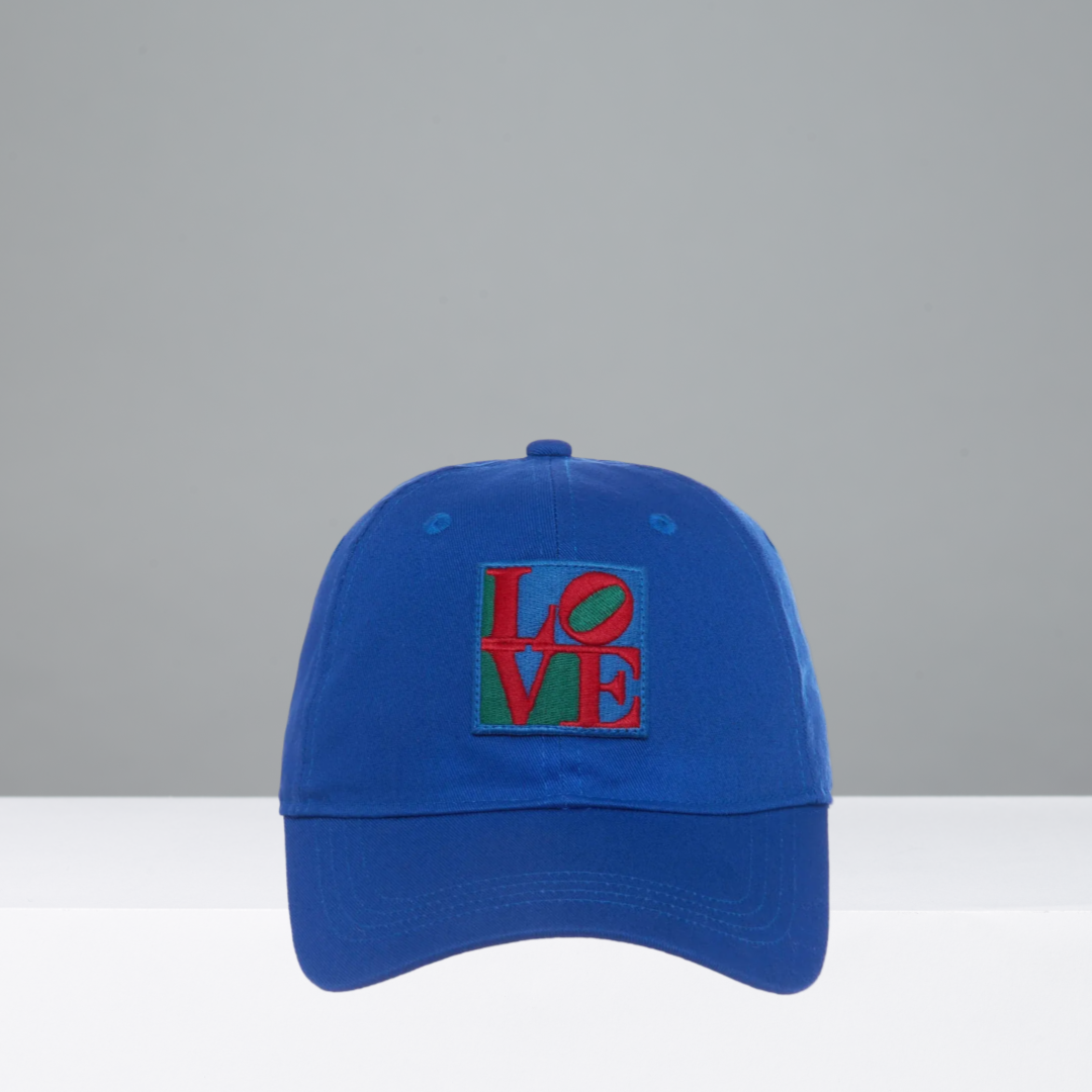 Blue colored cap with Robert Indiana's colorful 'LOVE' patch on a gray background