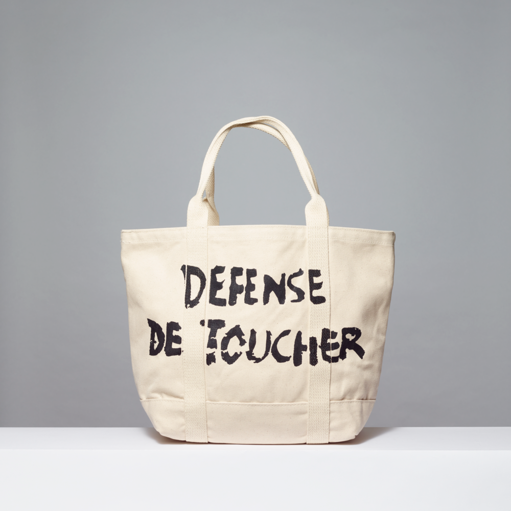 Beige tote bag with Defense de toucher in black text on a gray background
