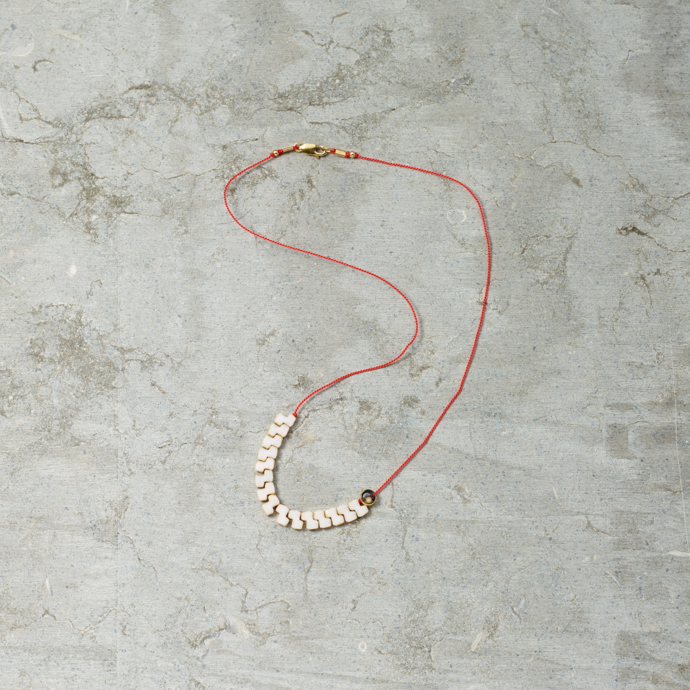 Necklace with red cord and white beads on a gray concrete surface
