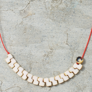 Necklace with white beads and a red cord on a textured gray surface