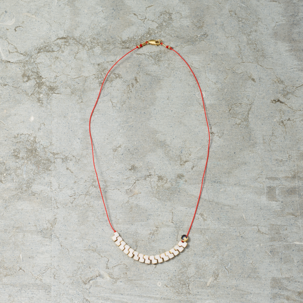 Necklace with red cord and white beads on a gray concrete surface