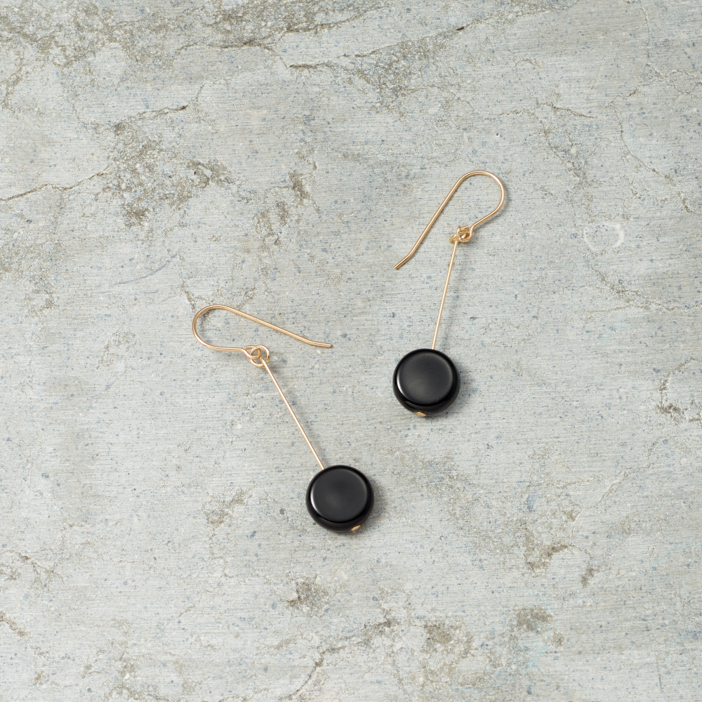 Pair of black earrings with gold hooks on a textured gray surface