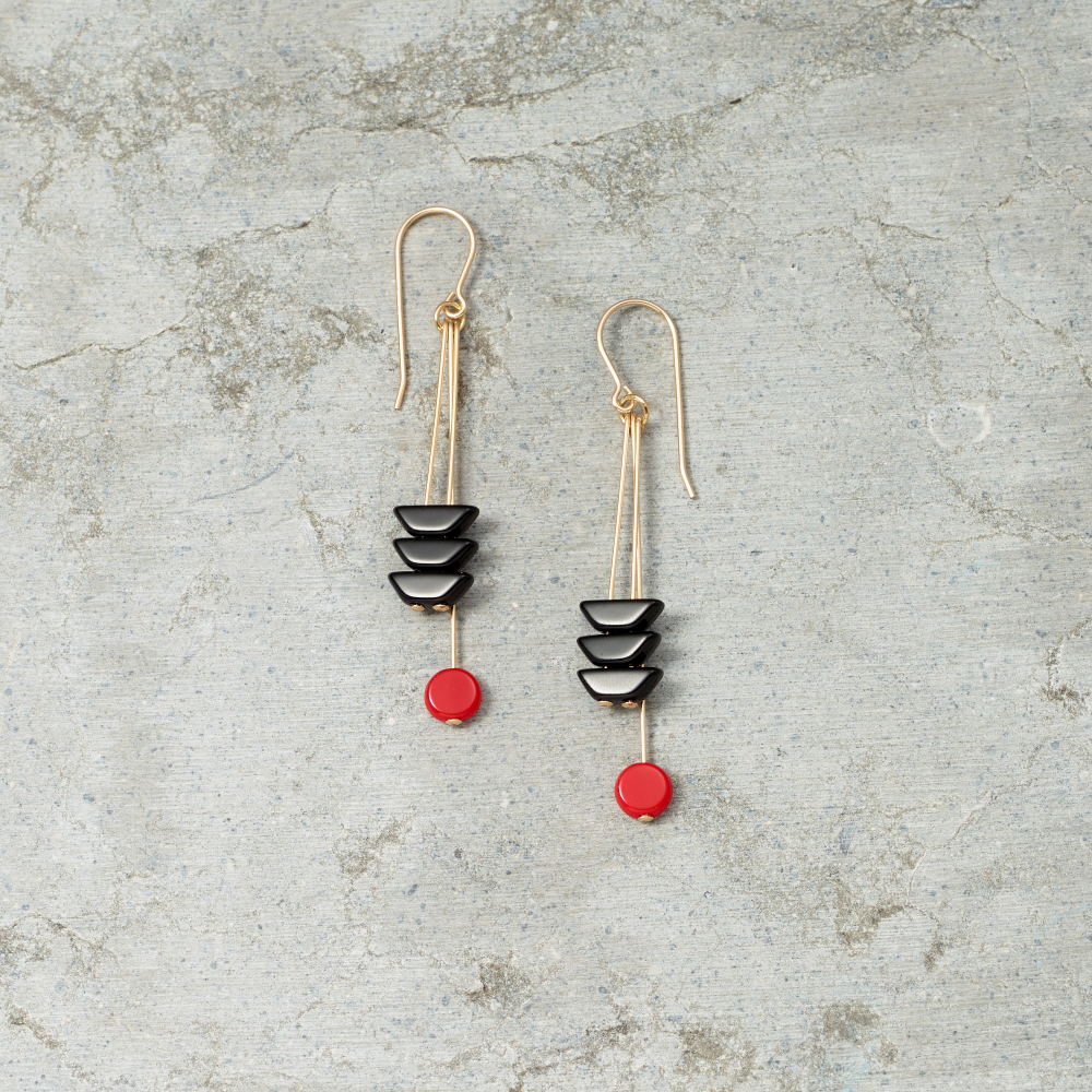 Pair of earrings with black and red stones on a textured gray surface