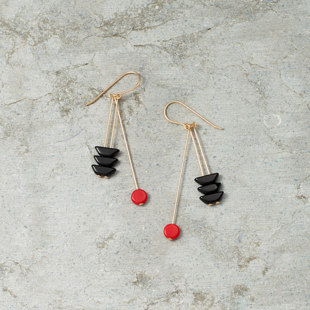 Pair of earrings with black and red stones on a textured gray surface