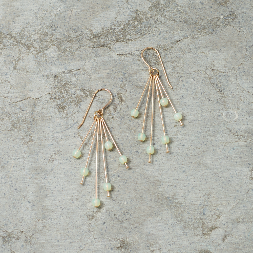 Gold earrings with green beads on a textured gray surface