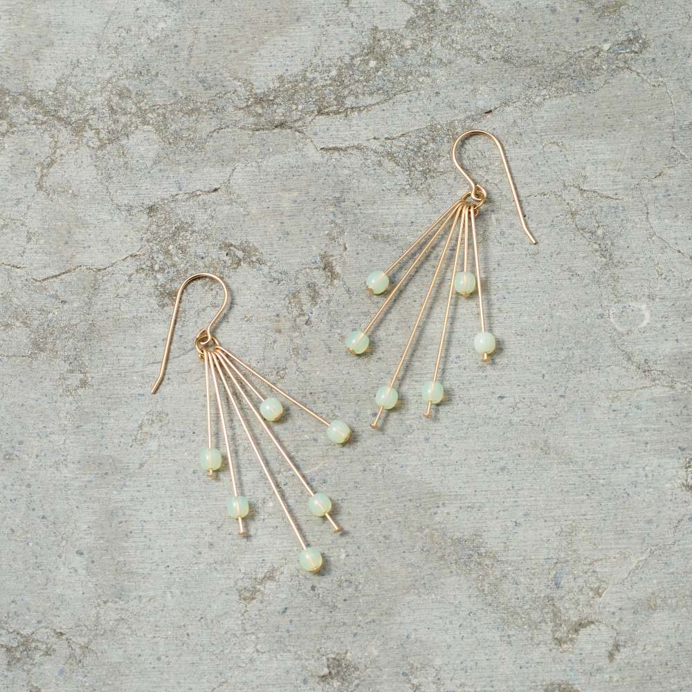 Gold earrings with green gemstones on a textured gray surface