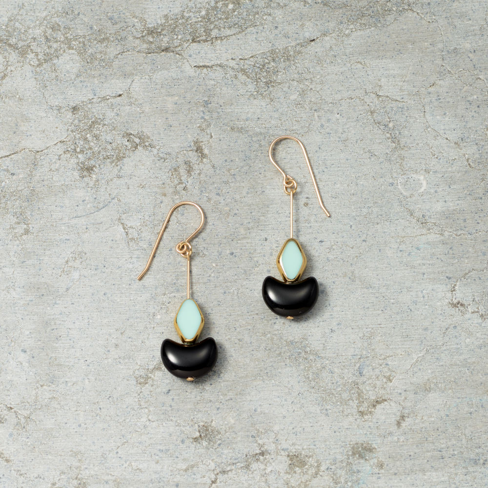 Pair of earrings with black and light blue stones on a textured gray surface