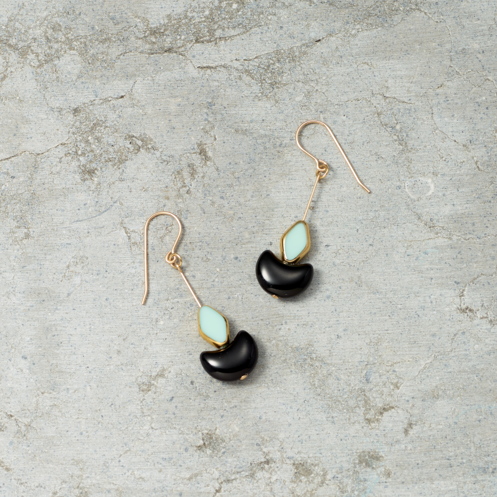 Pair of earrings with black and turquoise stones on a textured gray surface
