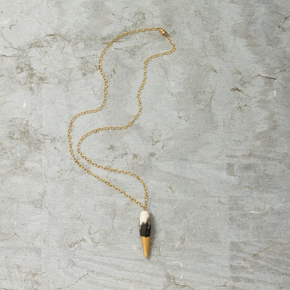 Gold necklace with a unique pendant on a textured gray surface