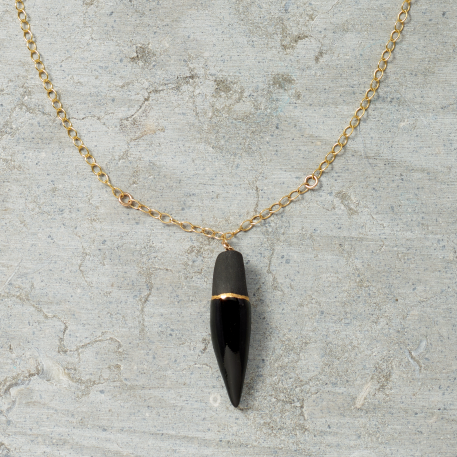 Black pendant necklace with gold chain on a gray surface