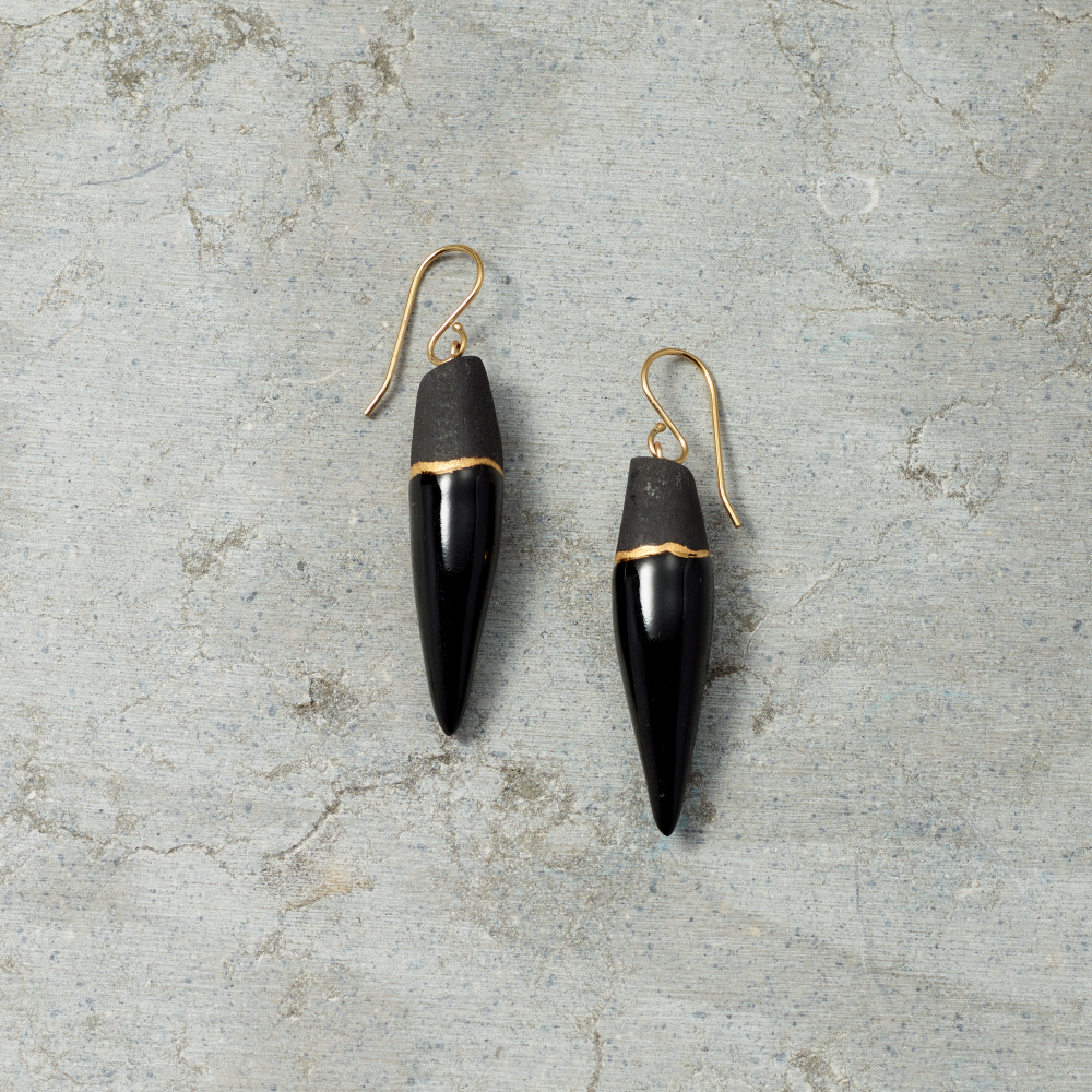 Black earrings with gold accents on a textured gray surface