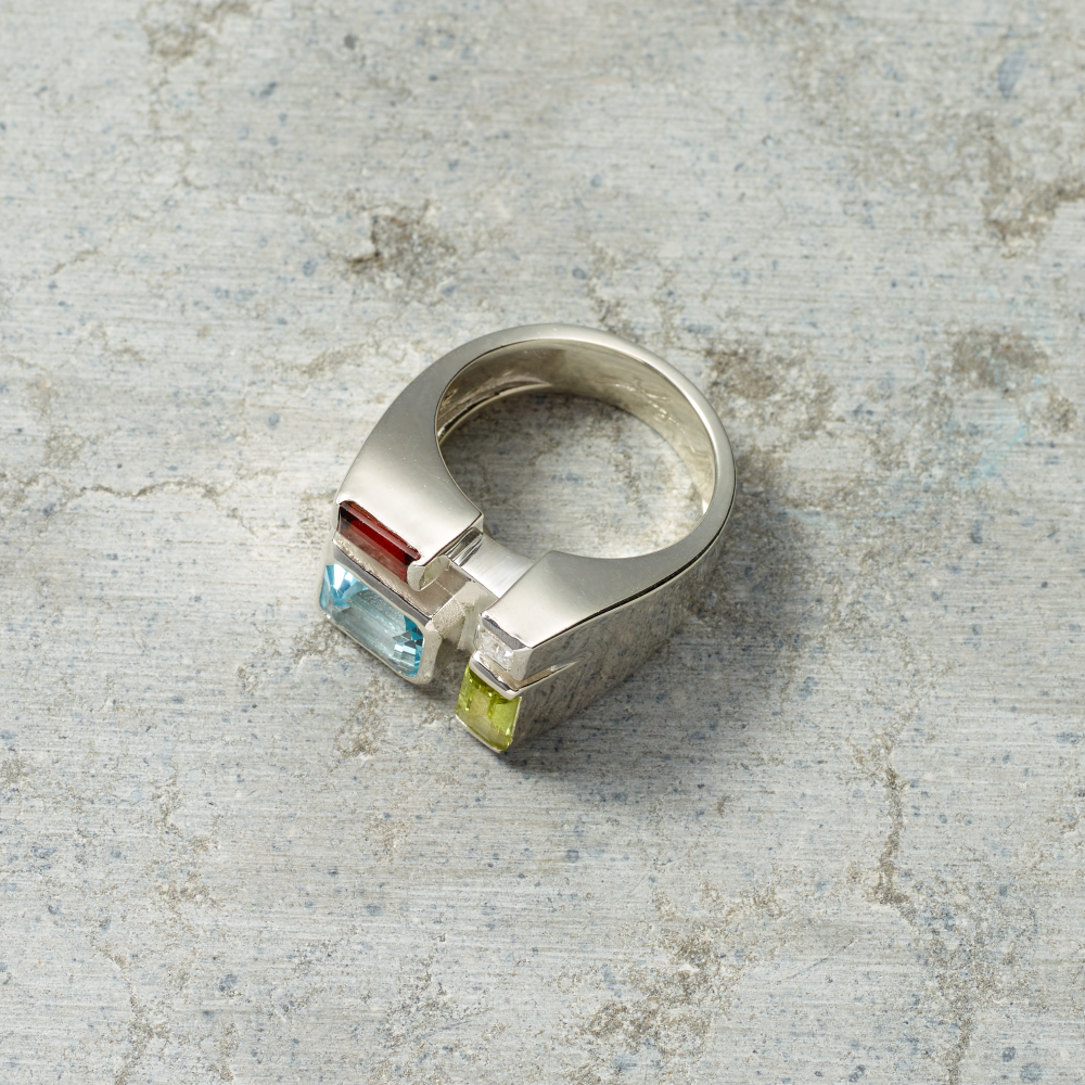 Silver ring with colorful gemstones on a textured gray surface
