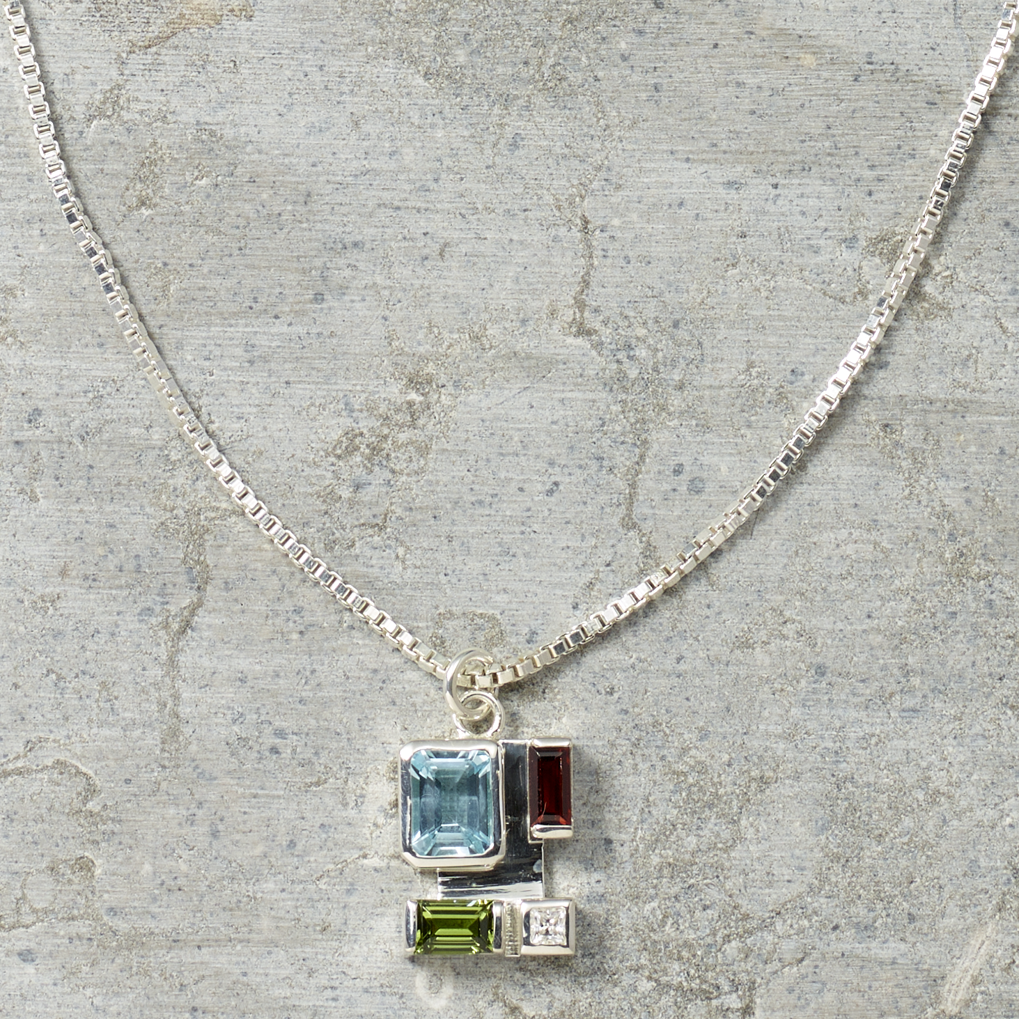 Necklace with a pendant featuring blue, green, and red gemstones on a textured surface.