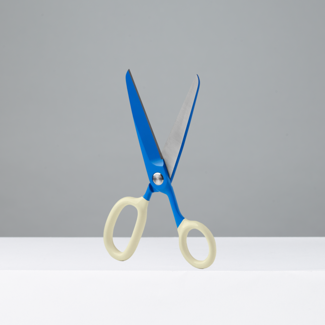 Blue and cream-colored scissors standing upright on a white surface against a light gray background.